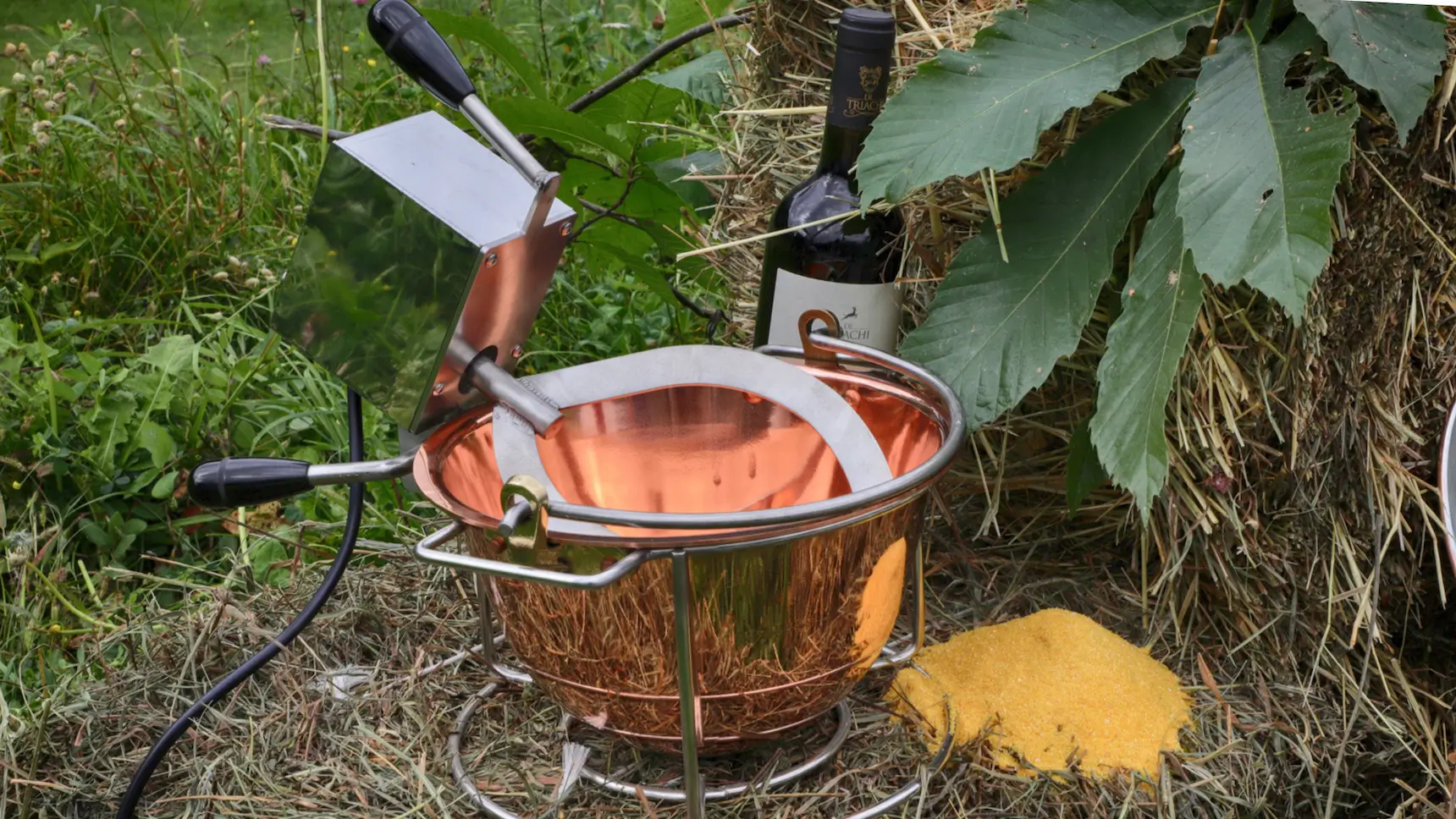 Polentina in rame con motore elettrico appoggiata su una balla di fieno e foglie di castano e bottiglia di vino