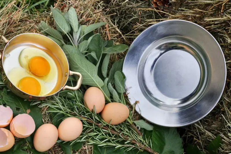 Tegame in rame con due uova crude, uova fresche, foglie di salvia e balle di fieno